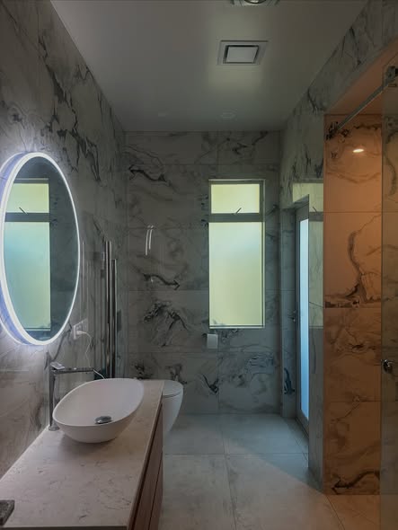 Marble walled bathroom with backlit round mirror